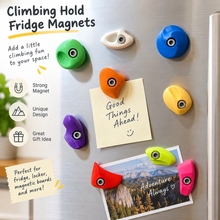 Colourful miniature climbing hold fridge magnets displayed on a refrigerator holding notes and a mountain postcard.
